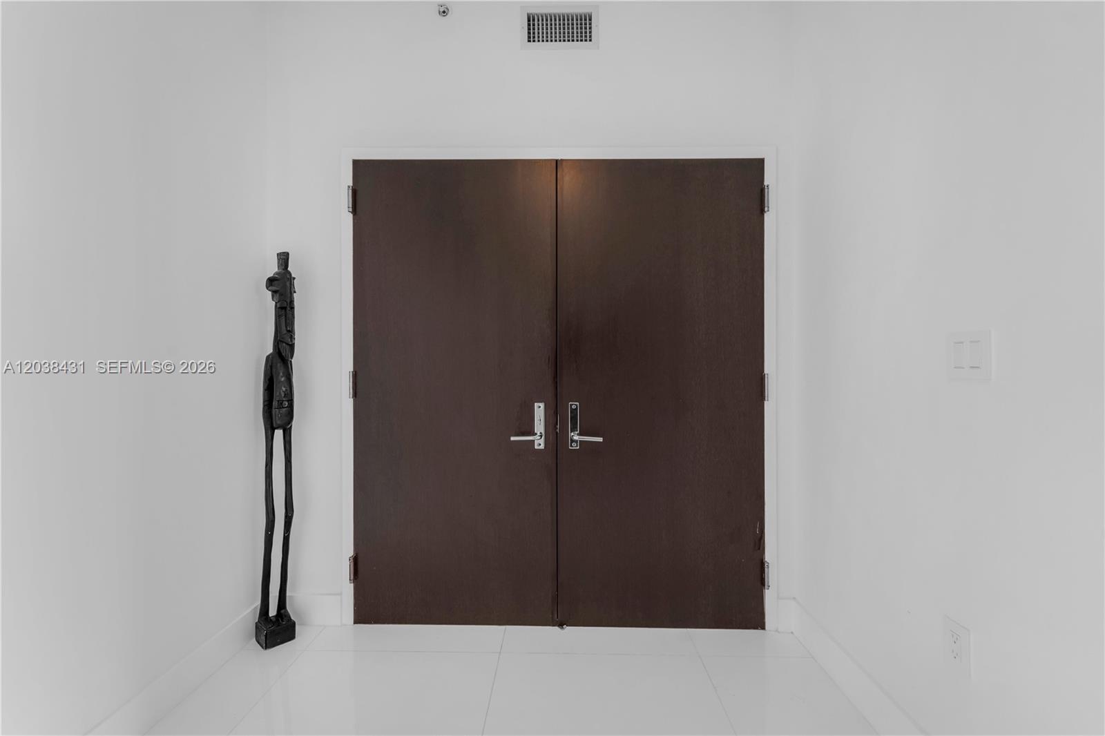 A tall wooden sculpture stands beside a set of dark double doors in a hallway — 900 Biscayne Blvd # 2302, Miami FL 33132, MIAMI, FL