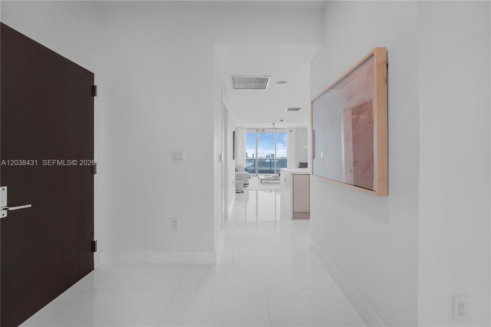 A white hallway with a dark door leads to an open living area with balcony views — 900 Biscayne Blvd # 2302, Miami FL 33132, MIAMI, FL