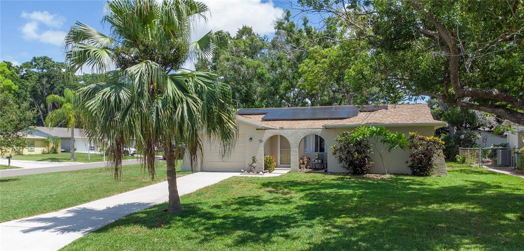 A single-story house with a tan stucco exterior, arched entryway, and solar panels on the roof — 160 MEADOWLARK DRIVE, SAFETY HARBOR, FL