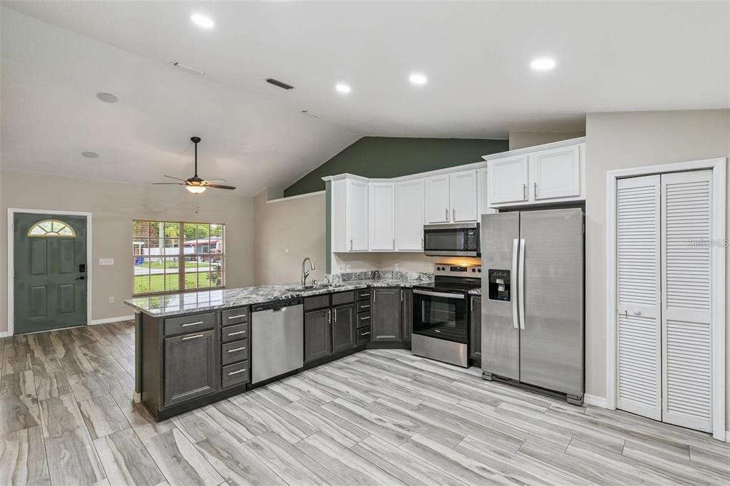 A kitchen with two-tone cabinetry, granite countertops, stainless steel appliances, and wood-look tile flooring — 1711 CHARLESTON LANE, ST CLOUD, FL