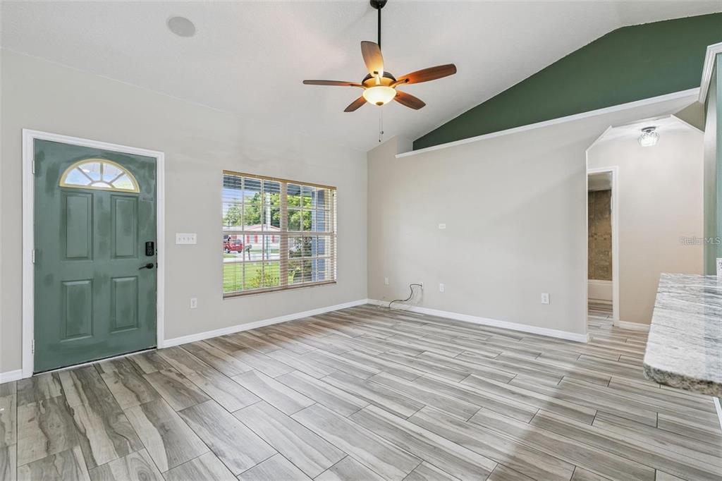 A living room features wood-look tile flooring, a vaulted ceiling, and a green front door — 1711 CHARLESTON LANE, ST CLOUD, FL