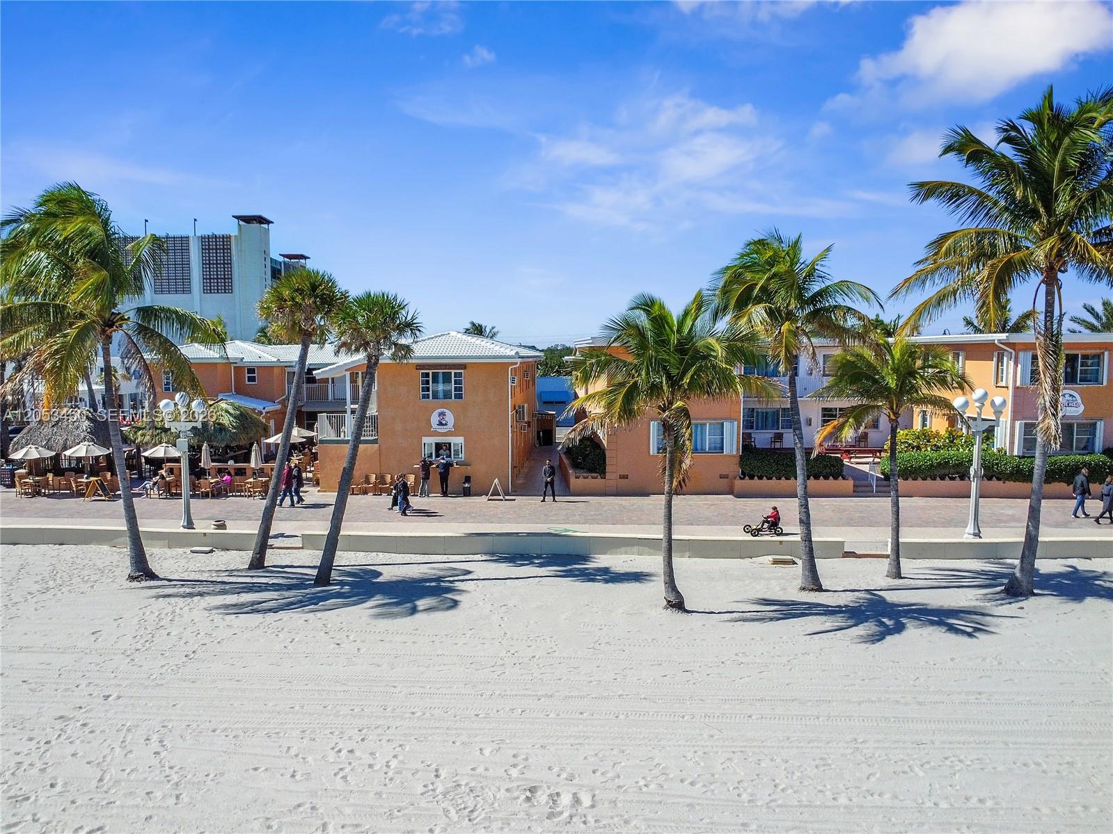 A sandy beach leads to a row of orange buildings with palm trees under a sky — 2300-2325 N Surf Rd, Hollywood FL 33019, HOLLYWOOD, FL