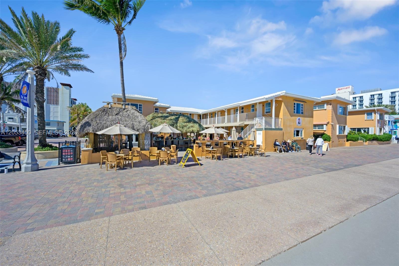 An outdoor patio area with tables and umbrellas sits in front of a yellow building — 2300-2325 N Surf Rd, Hollywood FL 33019, HOLLYWOOD, FL