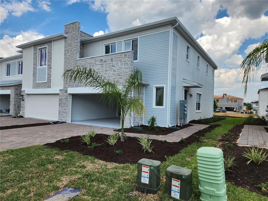 A two-story townhouse exterior features light blue siding, stone accents, and a covered parking area — 203 BOGEY DRIVE, DAVENPORT, FL