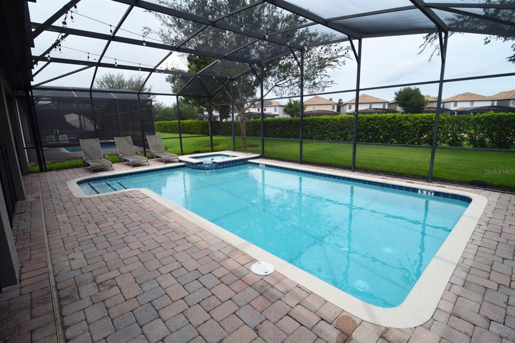 A rectangular swimming pool with an attached spa sits inside a screened-in brick patio — 1402 MOON VALLEY DRIVE, DAVENPORT, FL