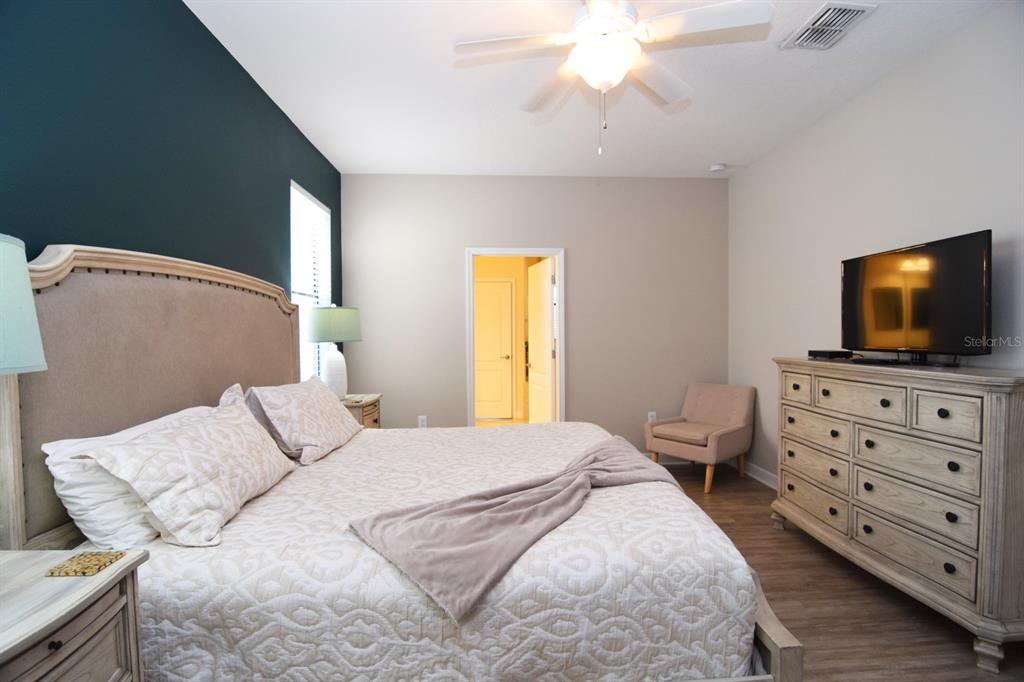A bedroom features a bed with a beige headboard, a dresser with a television, and flooring — 1402 MOON VALLEY DRIVE, DAVENPORT, FL