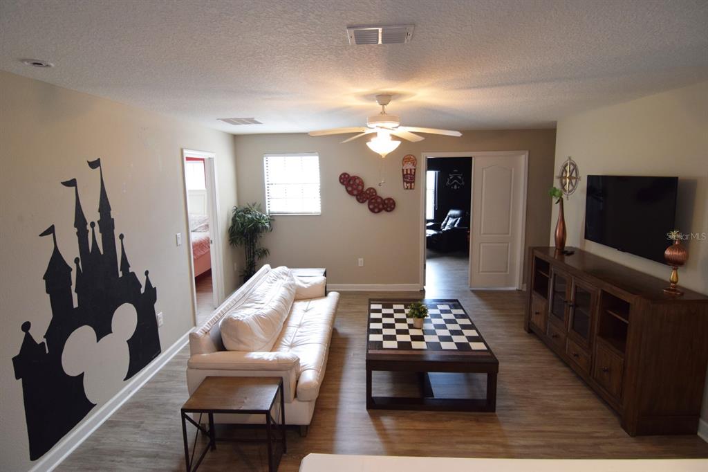 A living room features a white sofa, a checkerboard coffee table, and a Disney-themed wall decal — 1402 MOON VALLEY DRIVE, DAVENPORT, FL