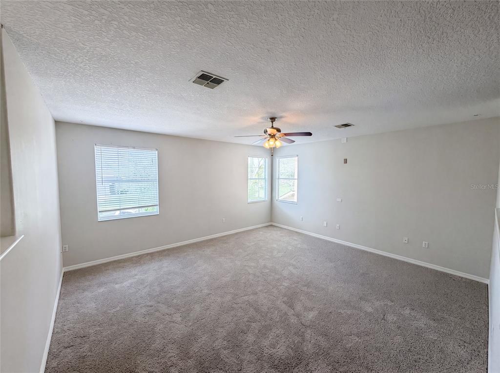 An empty room with gray carpet, light walls, a ceiling fan, and three windows — 12706 GROVEHURST AVENUE, WINTER GARDEN, FL