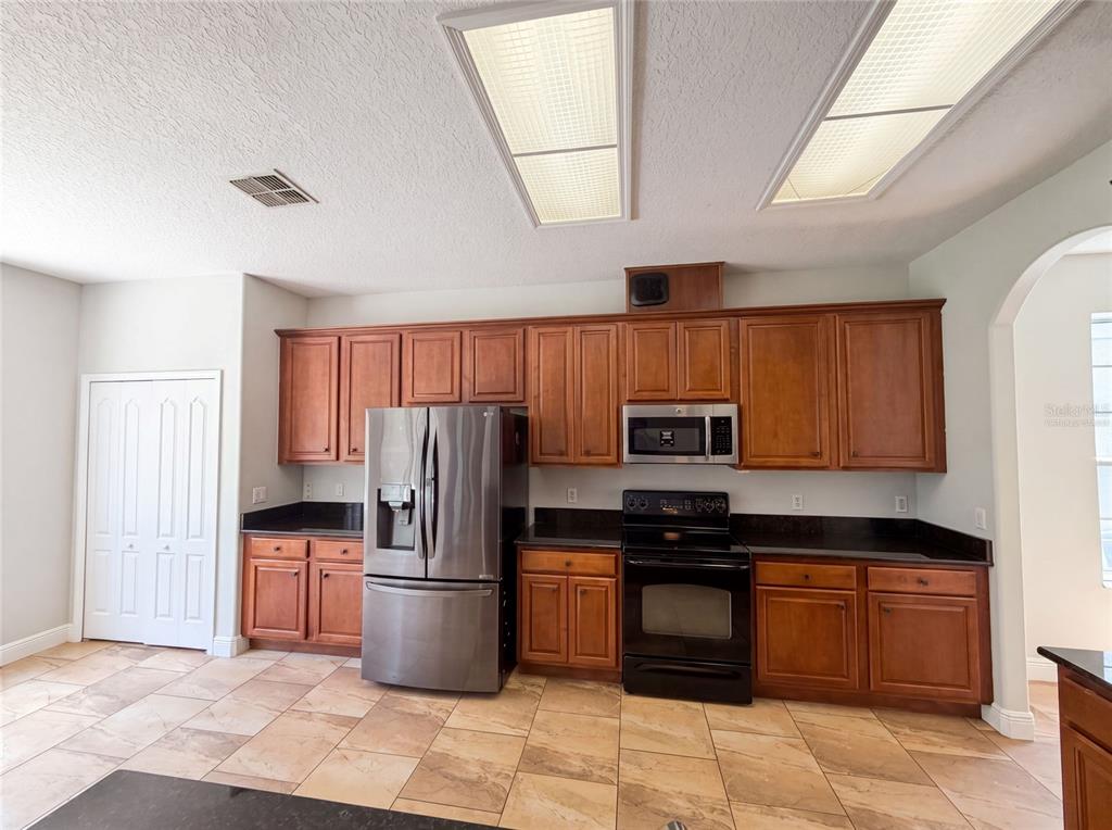 A kitchen features wood cabinets, stainless steel appliances, black countertops, and light-colored tile flooring — 12706 GROVEHURST AVENUE, WINTER GARDEN, FL