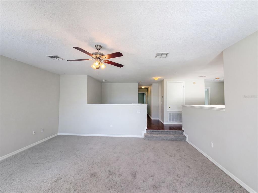 A carpeted living room features a ceiling fan, a half-wall, and a step-up hallway entrance — 12706 GROVEHURST AVENUE, WINTER GARDEN, FL