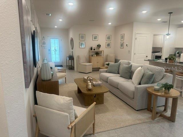 A bright living room features a light-colored sofa, wooden coffee table, and an entryway door — 1083 WELDA LANE, JACKSONVILLE, FL