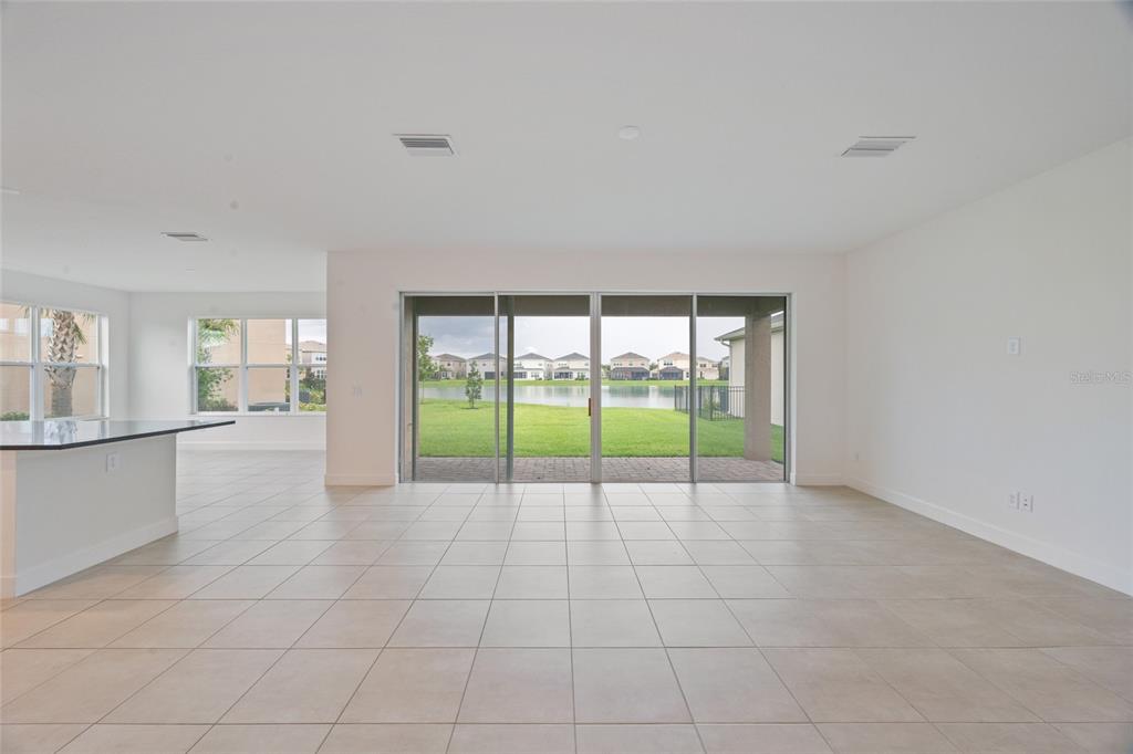 A bright, open-concept living area features large sliding glass doors overlooking a lake — 3488 GREAT BANYAN WAY, WESLEY CHAPEL, FL
