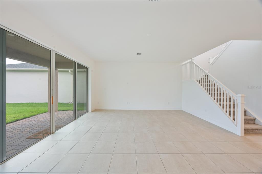 An empty room with light tile flooring, large sliding glass doors, and a carpeted staircase — 3488 GREAT BANYAN WAY, WESLEY CHAPEL, FL