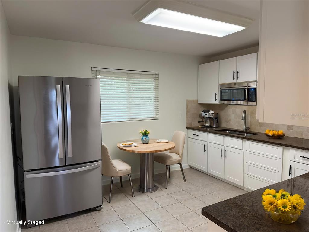 A kitchen features white cabinets, stainless steel appliances, a small dining table, and tile flooring — 1917 GILBERT STREET, CLEARWATER, FL