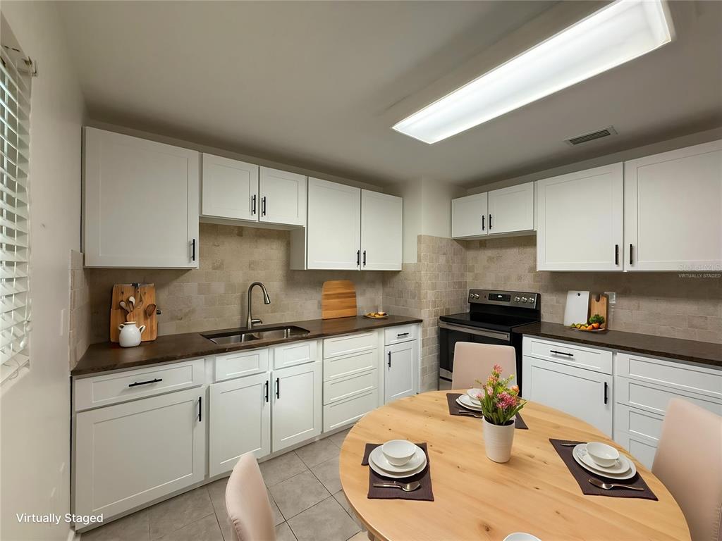 A kitchen with white cabinets, dark countertops, a tiled backsplash, and a round dining table — 1917 GILBERT STREET, CLEARWATER, FL