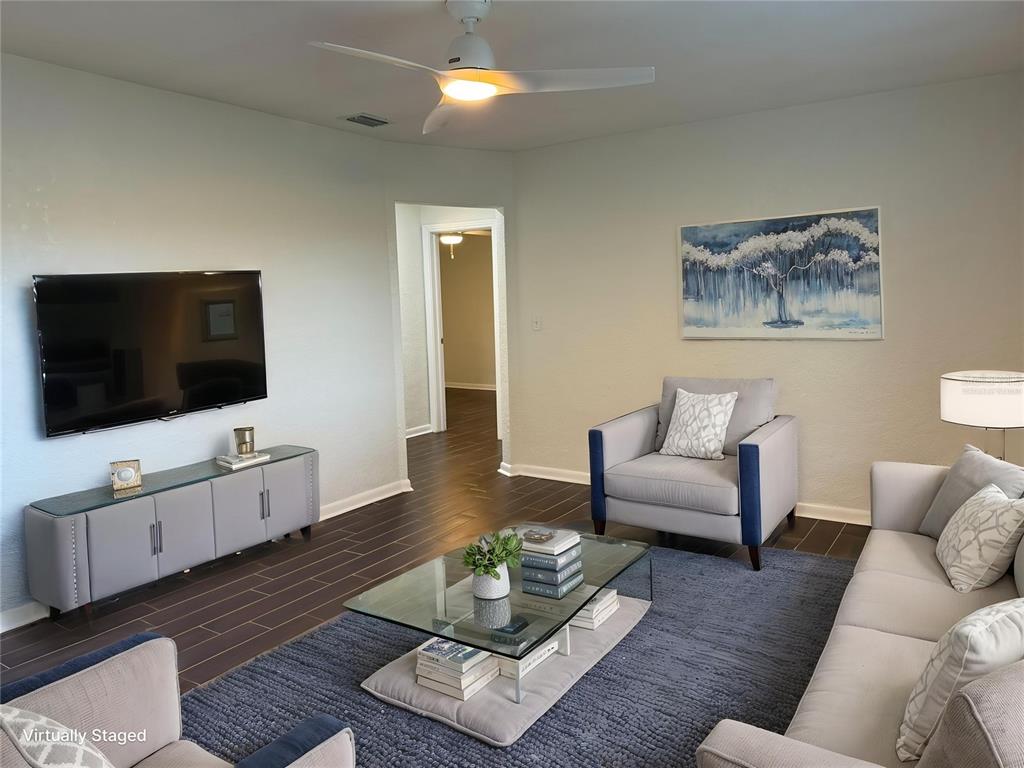 A living room features a television, gray furniture, a glass coffee table, and dark flooring — 1917 GILBERT STREET, CLEARWATER, FL