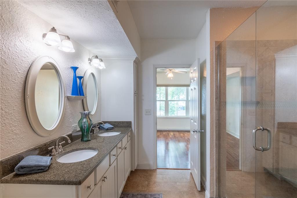 A bathroom features a double vanity with granite countertops, oval mirrors, and a glass shower — 202 E SOUTH STREET UNIT 1044, ORLANDO, FL