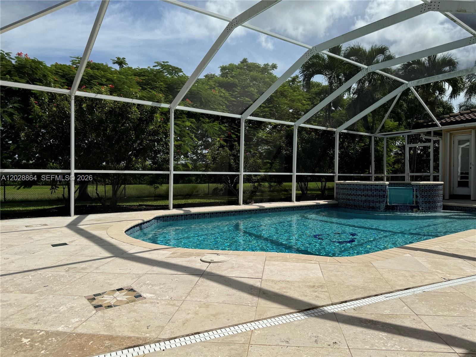 A screened-in swimming pool with a tiled water feature sits on a stone patio — WESTON, FL