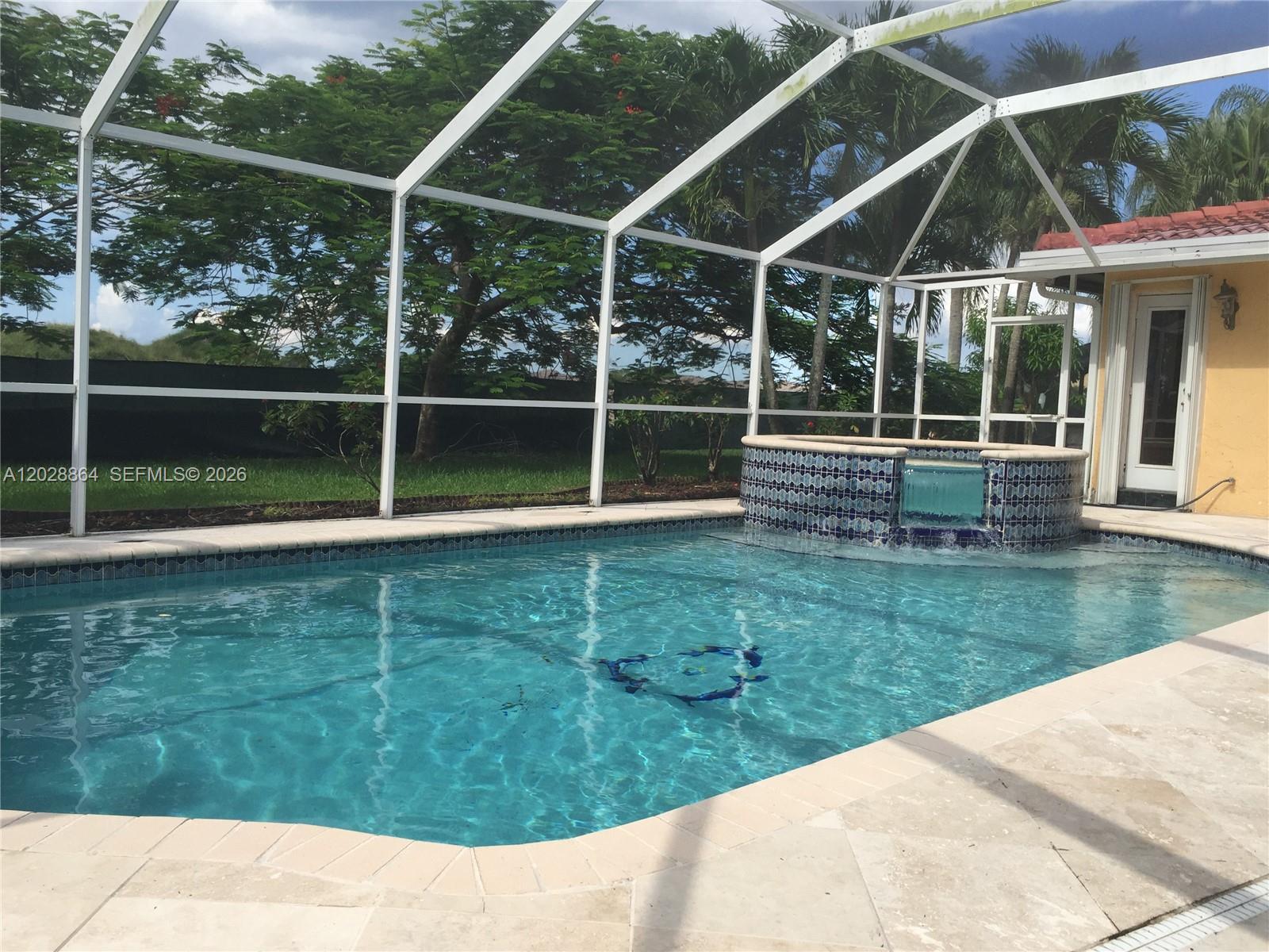 A screened-in swimming pool features a raised tiled spa with a waterfall spillway — WESTON, FL