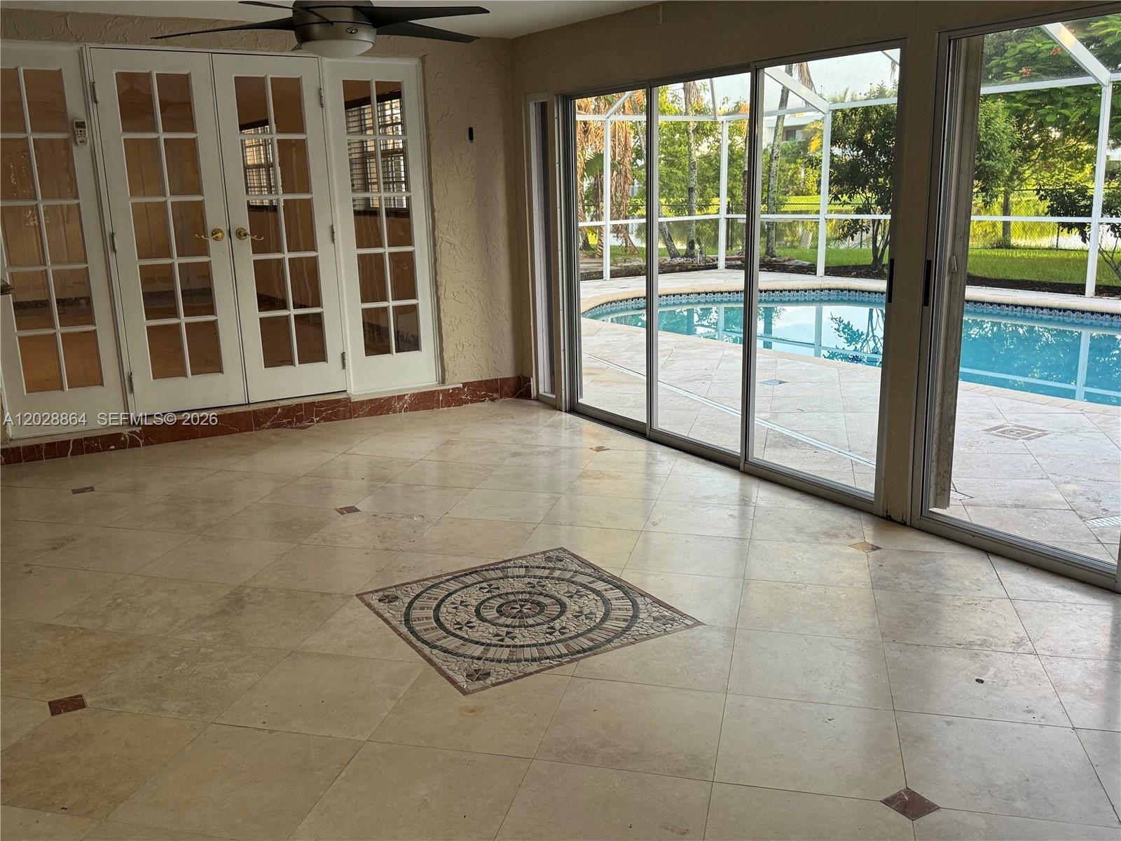 A sunroom with tiled floors, a decorative mosaic inlay, and sliding glass doors overlooking a pool — WESTON, FL