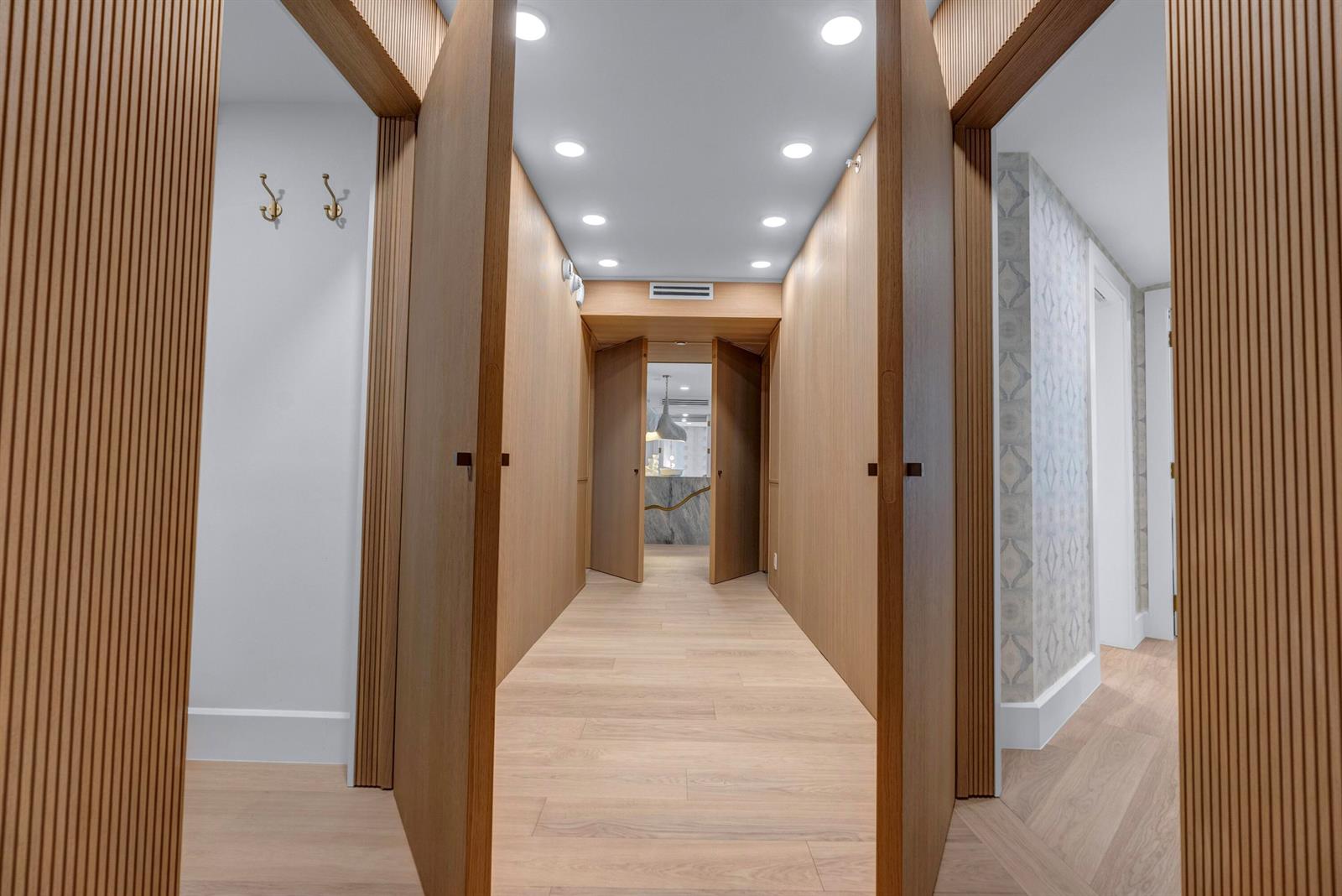 A hallway with light wood flooring and paneled walls leads to an open doorway — 3170 S Ocean Boulevard # N204, Palm Beach FL 33480, PALM BEACH, FL