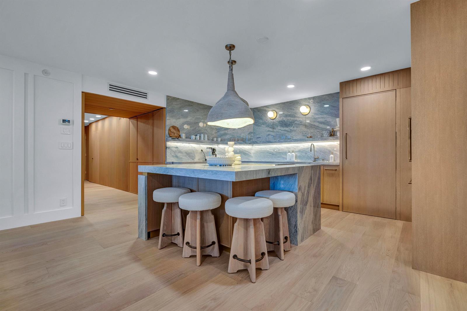 A modern kitchen features a stone island with four stools and wood-paneled cabinetry — 3170 S Ocean Boulevard # N204, Palm Beach FL 33480, PALM BEACH, FL