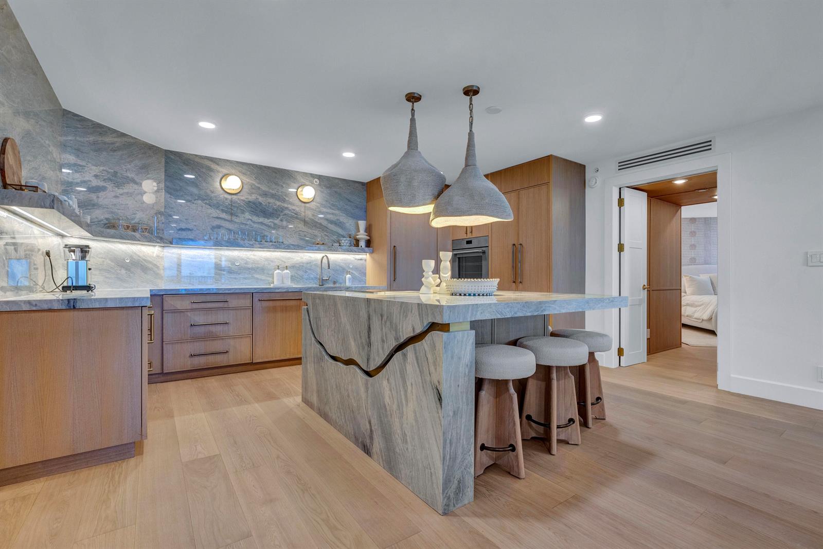 A modern kitchen features a stone island with a decorative cutout, wood cabinetry, and pendants — 3170 S Ocean Boulevard # N204, Palm Beach FL 33480, PALM BEACH, FL
