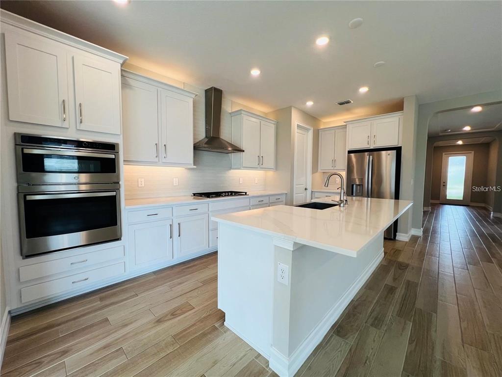 A modern kitchen features white cabinetry, stainless steel appliances, and a large quartz-topped island — 4567 TIVOLI DRIVE, WESLEY CHAPEL, FL