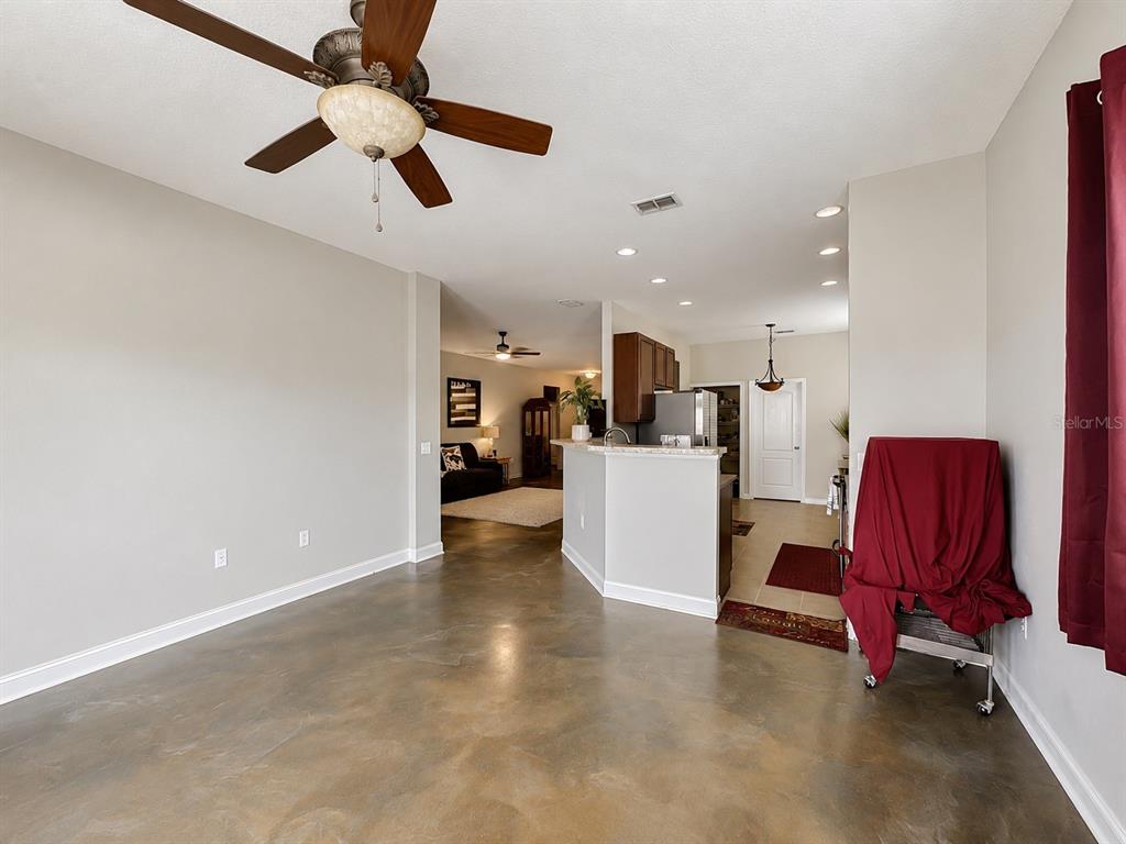 A living area with concrete floors and a ceiling fan opens to a kitchen area — 1012 SW 242ND TERRACE, NEWBERRY, FL