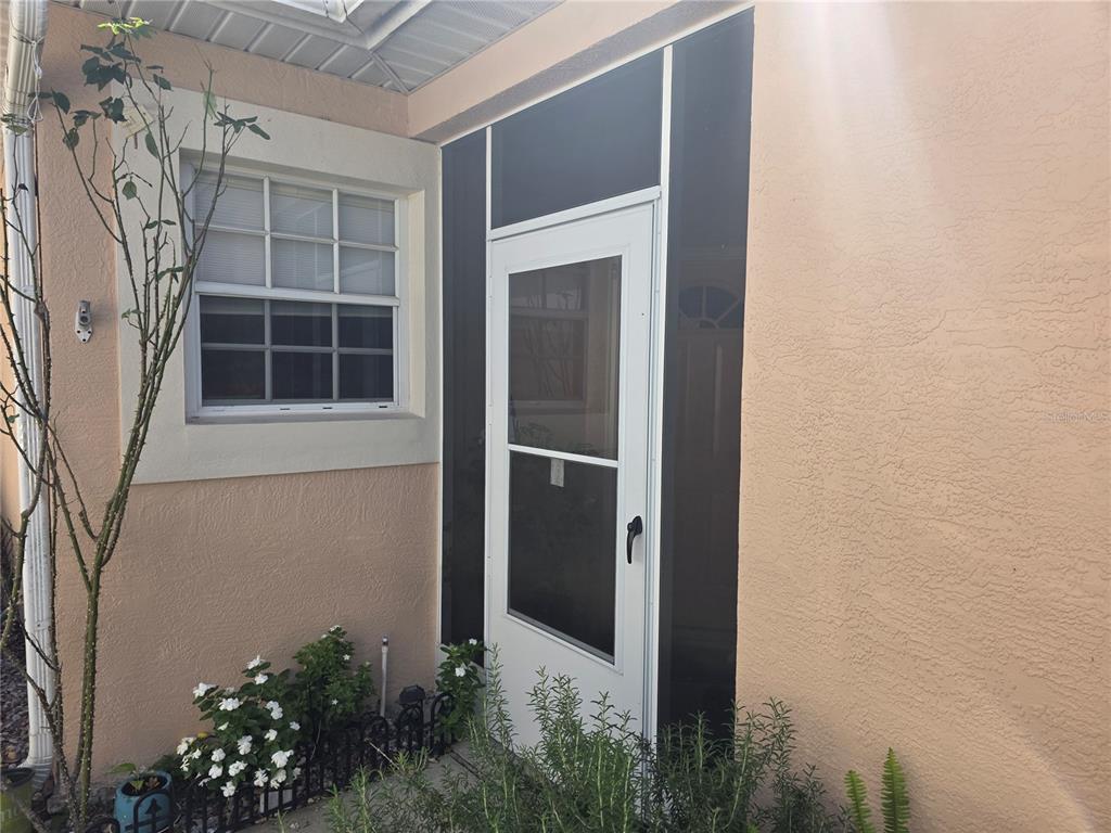 A white storm door with black screen panels is set into a peach-colored exterior wall — 322 FOXHILL COURT, DEBARY, FL