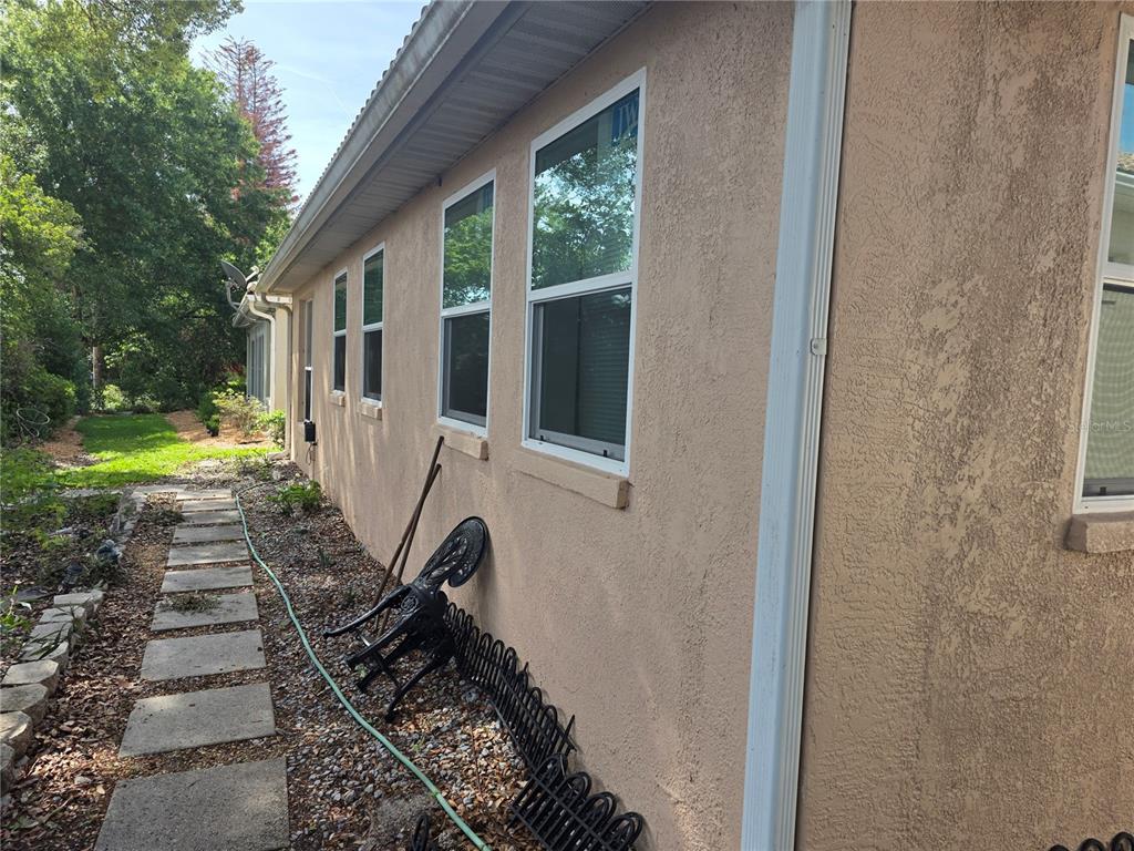 The exterior side of a tan stucco house features several windows and a white downspout — 322 FOXHILL COURT, DEBARY, FL