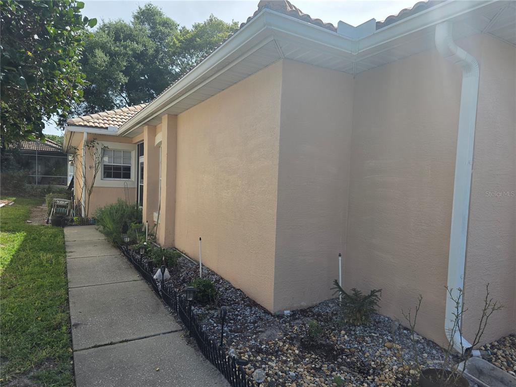 A beige stucco house exterior features a concrete walkway and a gravel garden bed — 322 FOXHILL COURT, DEBARY, FL
