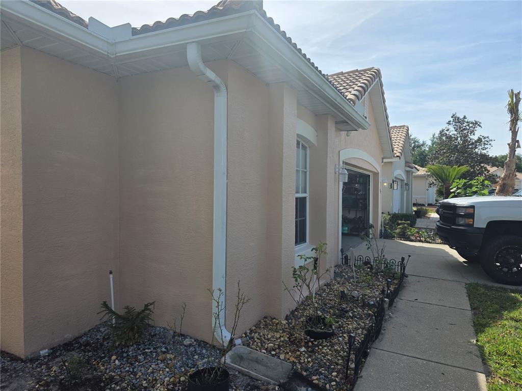 The exterior of a beige stucco house features a white downspout and a rock garden — 322 FOXHILL COURT, DEBARY, FL