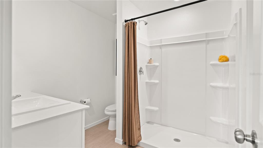 A bathroom features a white vanity, a toilet, and a shower stall with a curtain — 3416 ROVER ROAD, EAGLE LAKE, FL