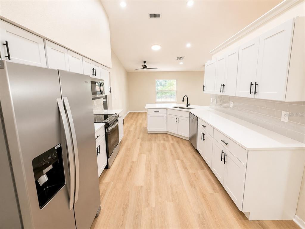 A kitchen with white cabinets, stainless steel appliances, and light wood-look flooring — 17440 SE 112TH AVENUE, SUMMERFIELD, FL