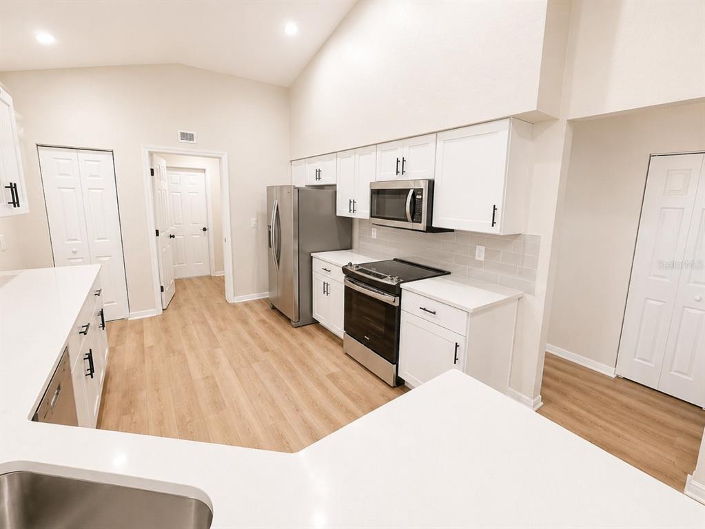 A kitchen with white cabinets, stainless steel appliances, and light wood-look flooring — 17440 SE 112TH AVENUE, SUMMERFIELD, FL