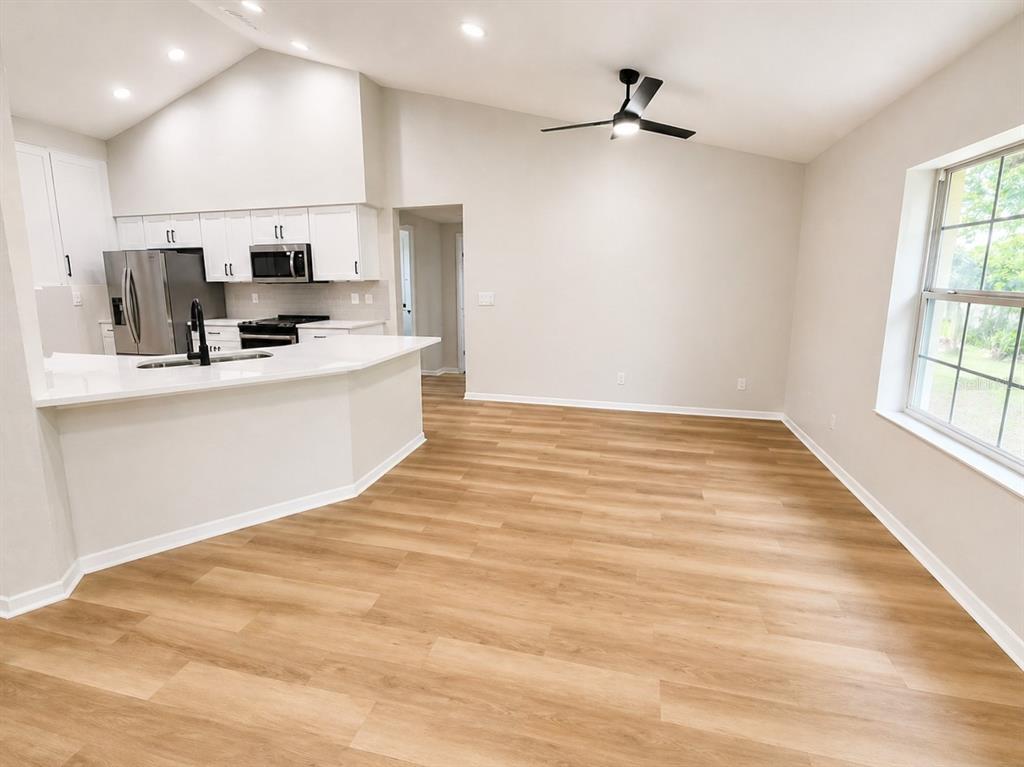 A kitchen with white cabinets and a breakfast bar opens into a spacious living area — 17440 SE 112TH AVENUE, SUMMERFIELD, FL
