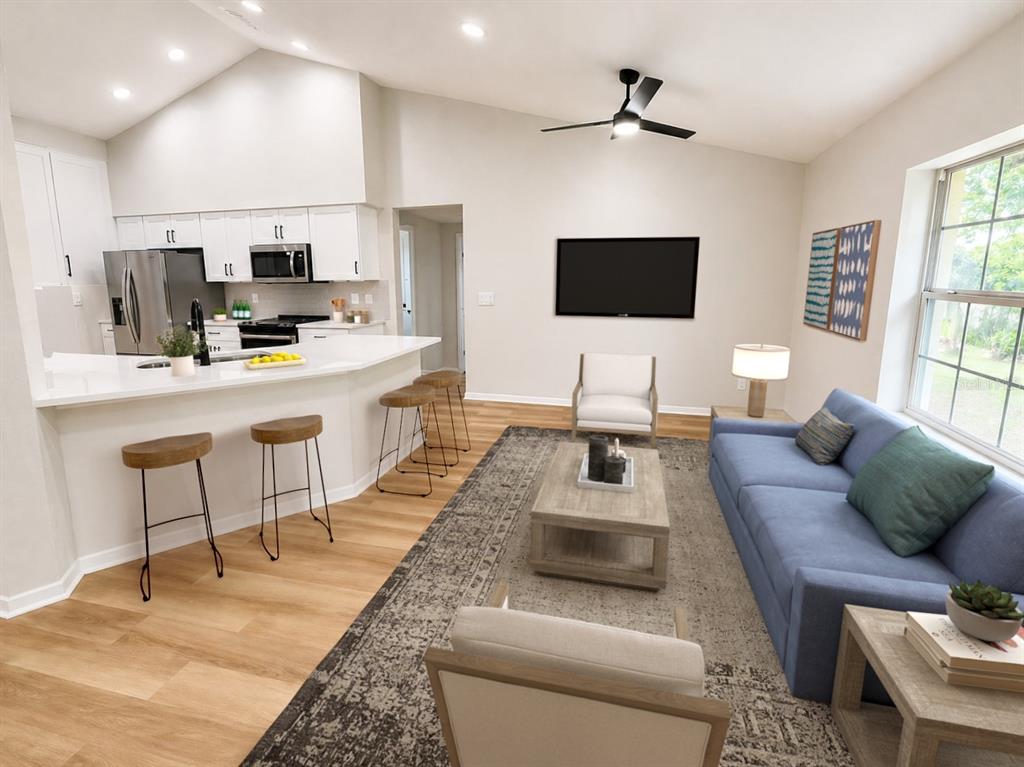 A modern open-concept living room and kitchen featuring white cabinetry, wood flooring, and blue sofa — 17440 SE 112TH AVENUE, SUMMERFIELD, FL