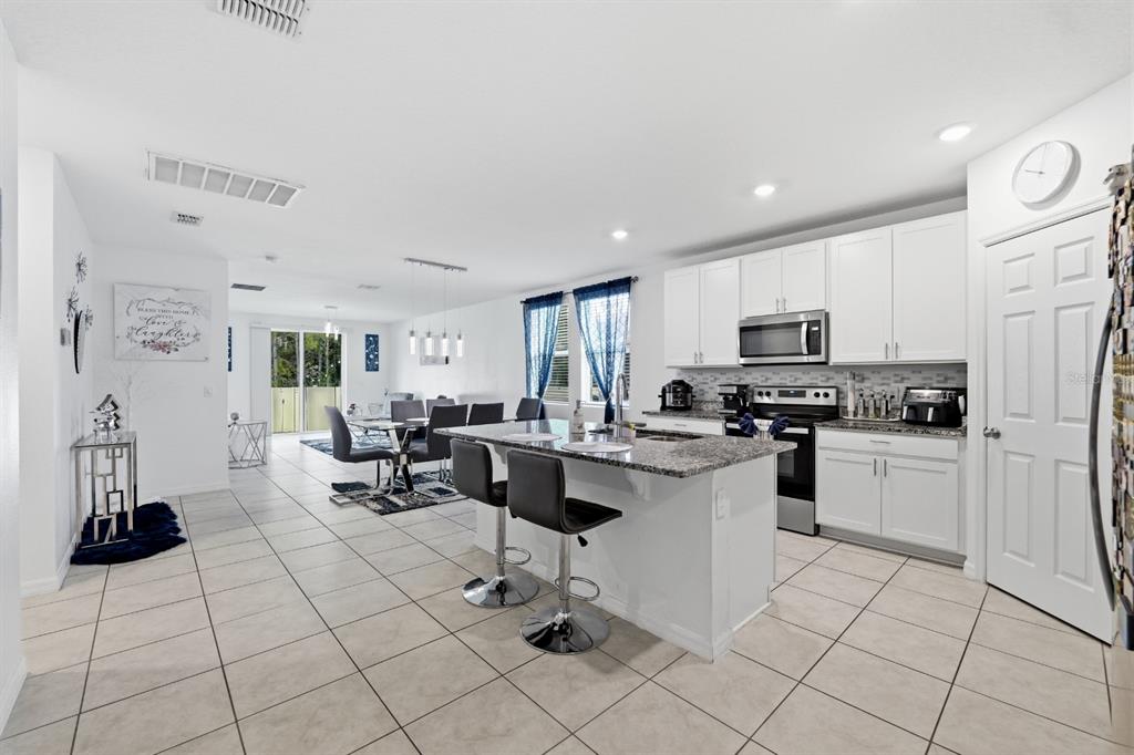 A kitchen with white cabinets and granite countertops opens into a dining and living area — 1036 KOBUK STREET, HAINES CITY, FL