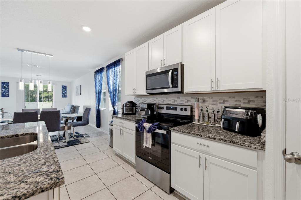 A kitchen with white cabinets, granite countertops, stainless steel appliances, and tile flooring — 1036 KOBUK STREET, HAINES CITY, FL