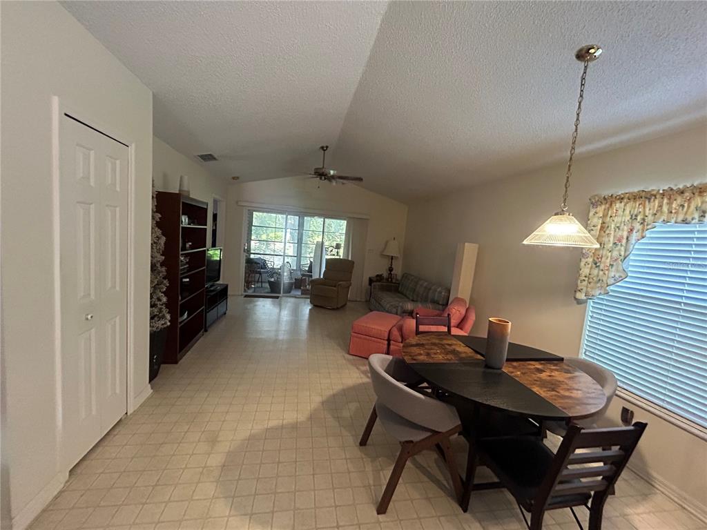A dining area and living room with vaulted ceilings, tile flooring, and a sliding glass door — 25119 CRANES ROOST CIRCLE, LEESBURG, FL