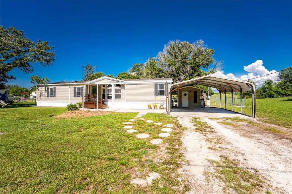 A single-story manufactured home features light siding, a front porch, and an attached metal carport — 5635 SW BRAHMA AVENUE, ARCADIA, FL
