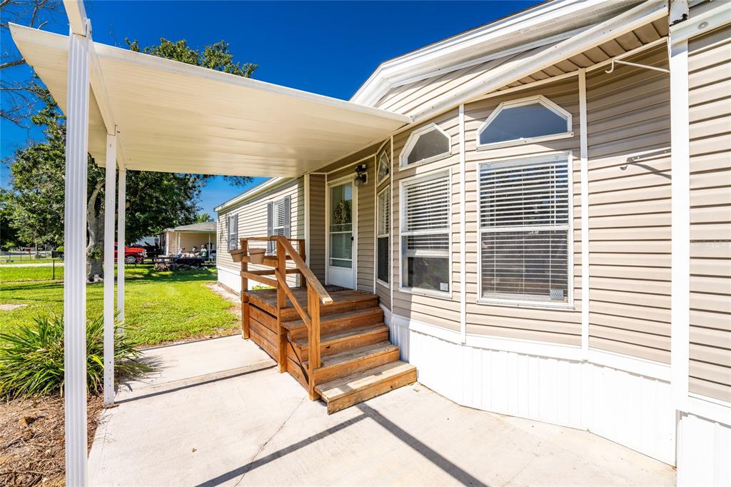 A mobile home exterior features a concrete patio, a covered carport, and wooden entry steps — 5635 SW BRAHMA AVENUE, ARCADIA, FL