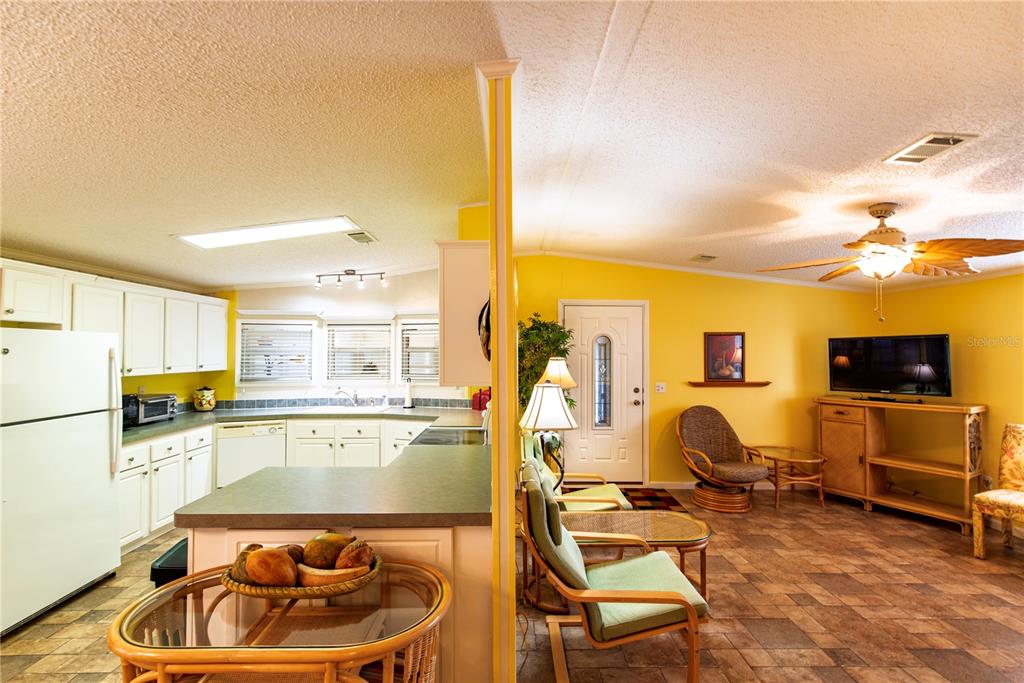 An open-concept kitchen and living area featuring yellow walls, tile flooring, and wicker furniture — 29 AMSTERDAM AVENUE, PUNTA GORDA, FL