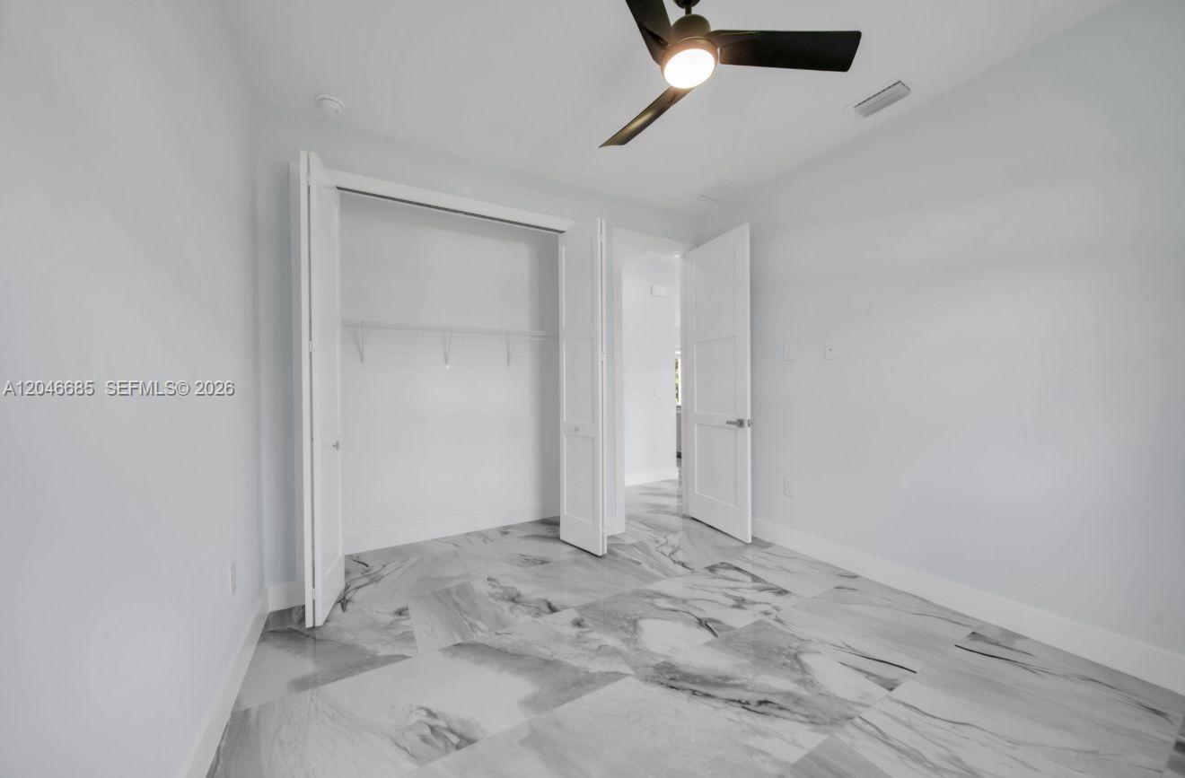 A bedroom features white walls, a ceiling fan, and light-colored marble-patterned tile flooring — 204 E 10th St, Lehigh Acres FL 33972, LEHIGH ACRES, FL