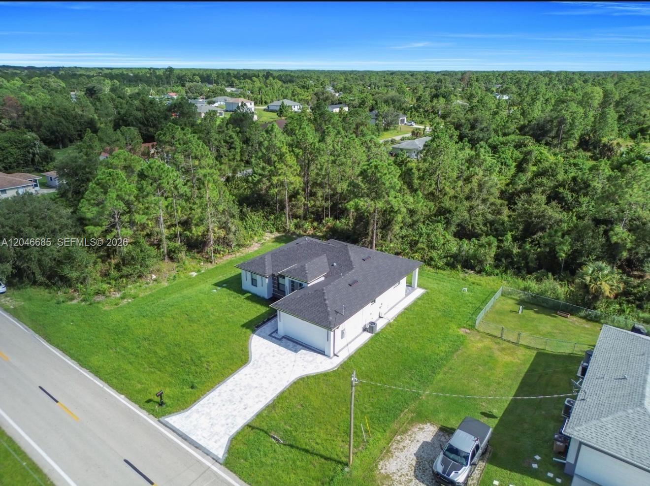 An aerial view shows a white house with a dark roof and a paved driveway — 204 E 10th St, Lehigh Acres FL 33972, LEHIGH ACRES, FL