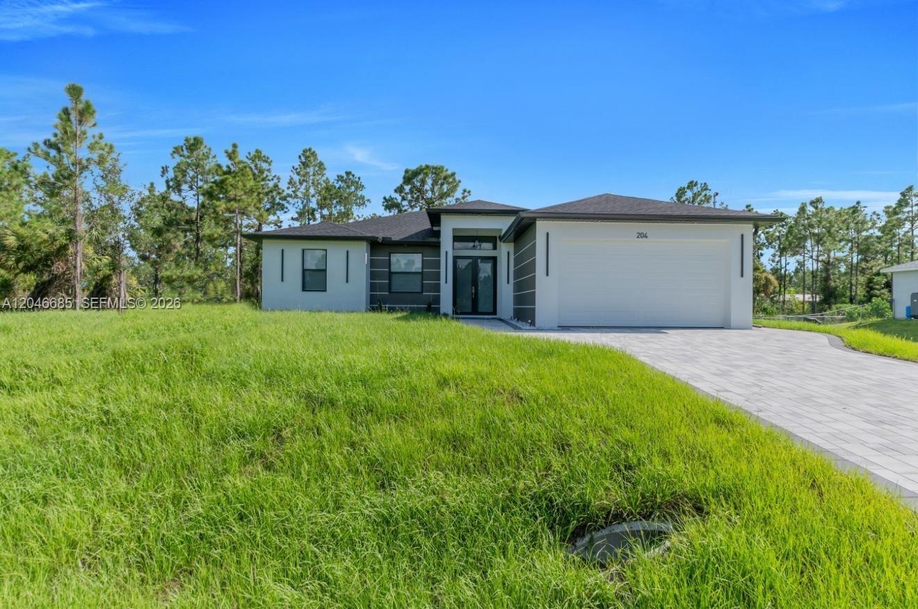 A modern single-story house with a white facade, dark accents, and a paved driveway — 204 E 10th St, Lehigh Acres FL 33972, LEHIGH ACRES, FL