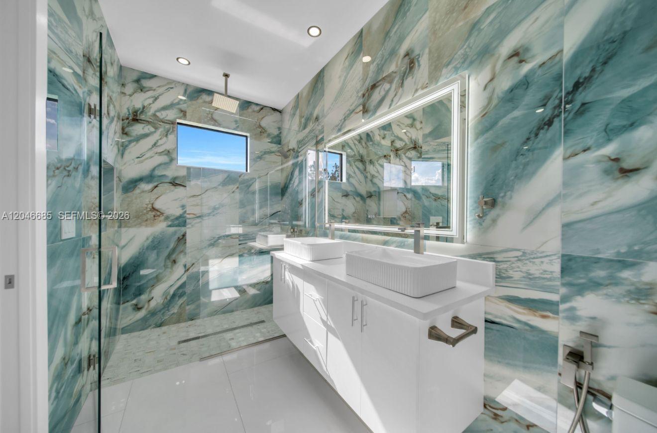 A modern bathroom features blue marble-patterned walls, a double vanity, and a glass-enclosed shower — 204 E 10th St, Lehigh Acres FL 33972, LEHIGH ACRES, FL