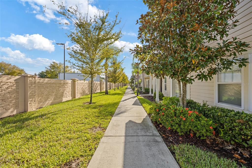 A concrete sidewalk runs between a stone-textured privacy wall and a row of residential buildings — 8945 SHINE DRIVE, KISSIMMEE, FL