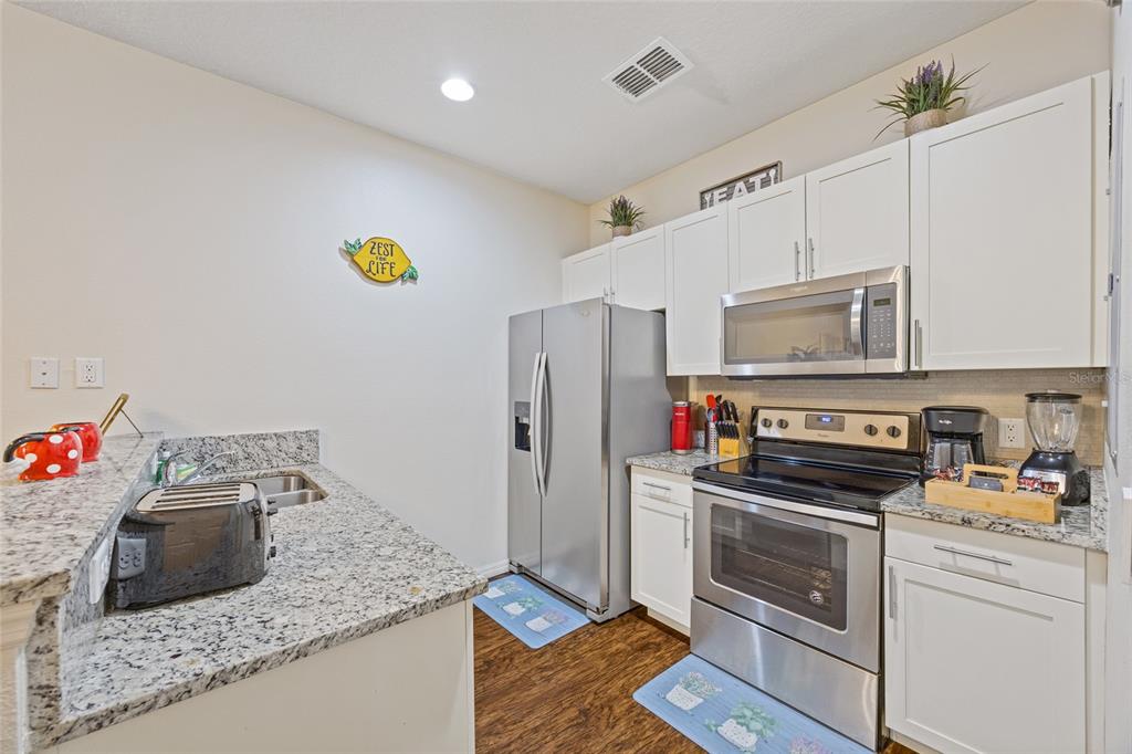 A kitchen features stainless steel appliances, white cabinetry, and granite countertops — 8945 SHINE DRIVE, KISSIMMEE, FL